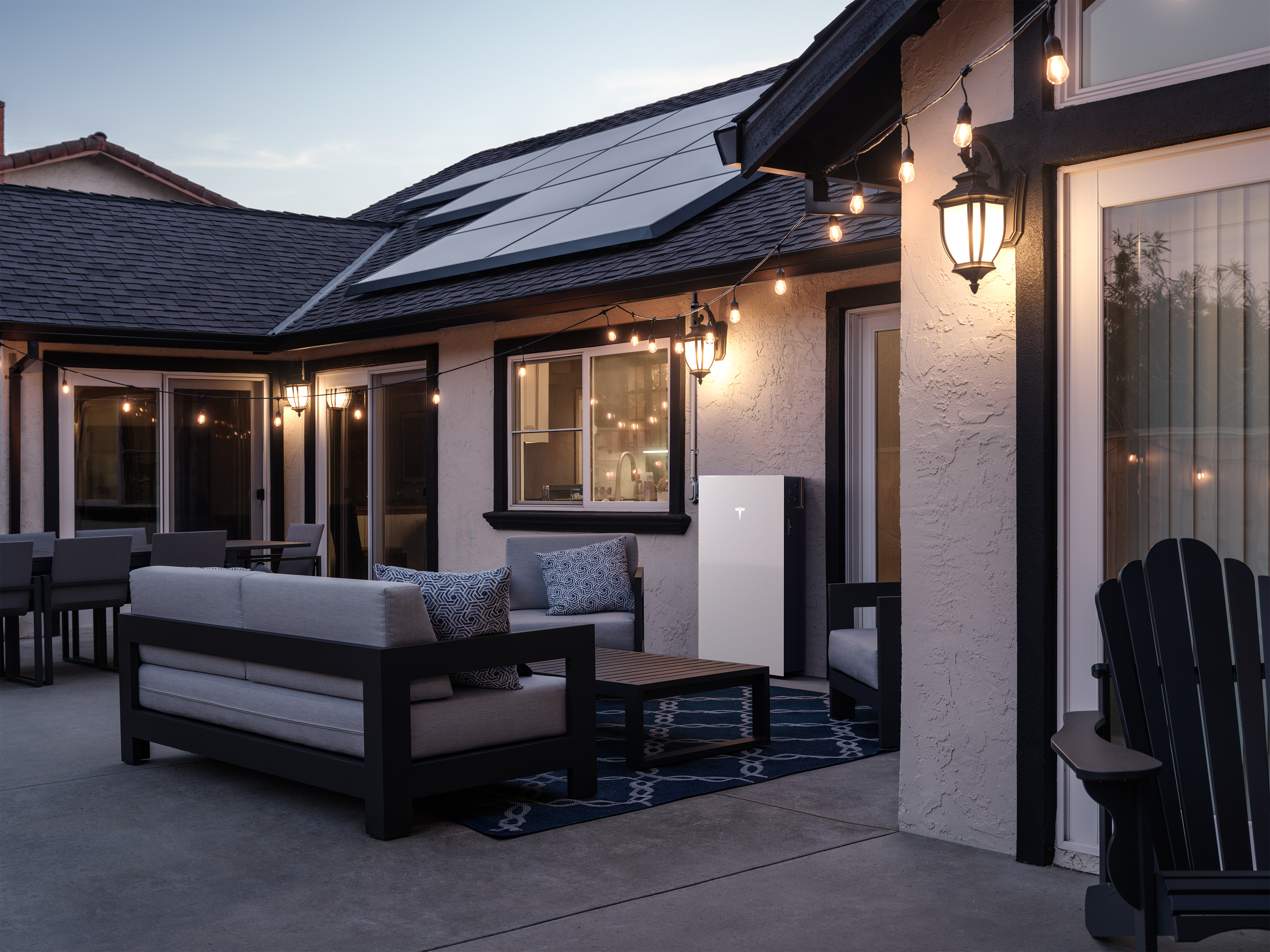 Photo of a home patio with solar on the roof and a Tesla Powerwall installed onto the exterior wall.